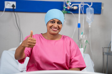 Happy smiling indian recovered breast cancer patient showing thumbs up by looking camera on bed at...