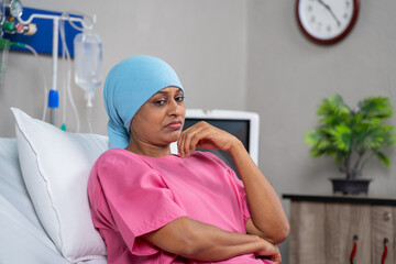 Thoughtful indian cancer patient deep thinking while sitting on bed at hospital - concept of...