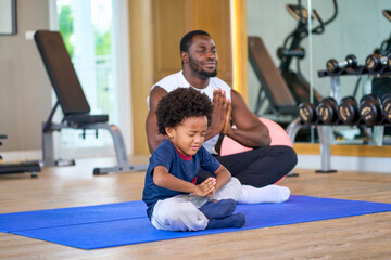 African american dad and son play yoga in fitness room for family activity together.