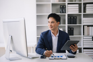Obraz na płótnie Canvas Confident Asian man with a smile standing holding notepad and tablet at the modern office.