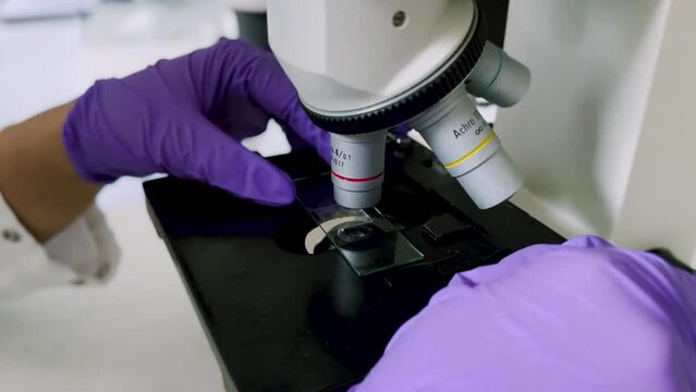 Close-up shot of microscope with metal lens at laboratory. Young woman scientist using microscope in laboratory. Close up of examining of test sample under the microscope in laboratory.