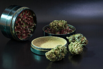 herb grinder full of cannabis pollen surrounded by dry flowers of medical marijuana close up on black background  - obrazy, fototapety, plakaty