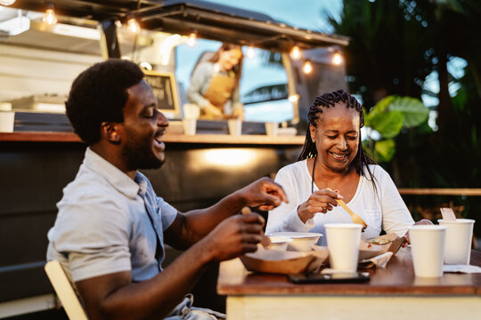 Happy African mother and son having fun eating in a street food truck market outdoor