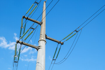 Reinforced concrete power line pole with insulators and wires against the blue sky