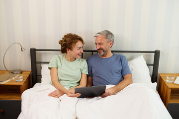 Smiling mature couple using digital tablet at home in bed