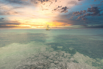 Panoramic view from the shoreline of a sailing ship sailing at sunrise in the South Seas. In the background the multicolored sky of French Polynesia.