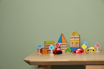 Set of different wooden toys on table near olive wall, space for text. Children's development