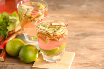Glasses of tasty rhubarb cocktail and lime fruits on wooden table, closeup. Space for text