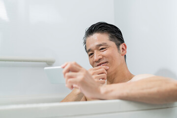 半身浴をしながらスマートフォンで動画を見る40代男性