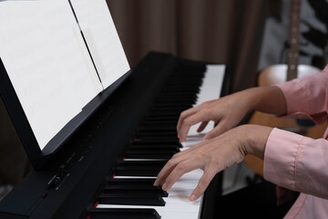 Obraz premium Close up woman hand playing piano at home. Relaxing time concept. Practicing music at home, White blank paper for note put on paino holder. Hands put on keyborad.