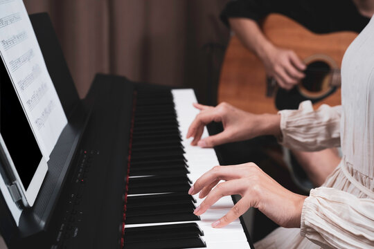 A woman hand pressed on paino keyboard while her friend playing guitar, playing music together at home, tablet and key note paper on paino holder. Relaxing time, practicing, learning music.