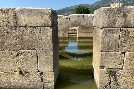 Ceiling ruins of ancient stone temple of Apollon in Klaros ancient city filled water, top arches and keystones with reflections under blue sky İzmir