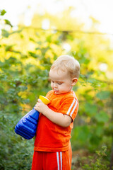 cute little boy in the garden with a toy container for watering plants, rural scene, child leisure on nature