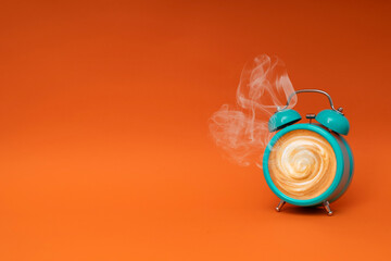 Hot coffee in a blue retro alarm clock on orange background. Waking up with alarm and coffee concept