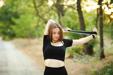 Young beautiful woman working out with fitness rubber bands in the forest, girl training hands, sport concept