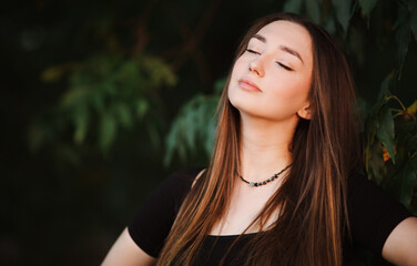 Naklejka premium beautiful young woman with closed eyes in dark green foliage, girl face on summer nature
