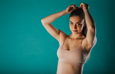 Fototapeta na wymiar A confident fit woman showcases her transformation - muscular arms, defined abs. Inspiring motivation on turquoise background.