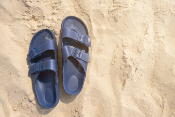 Fototapeta premium Pair of blue plastic buckled sandals or flip-flops on a beach sand with copy space