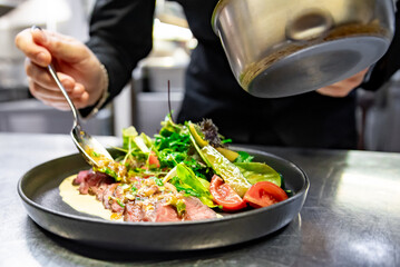 chef hand cooking Roast beef salad with vegetables on restaurant kitchen