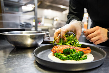 chef hand cooking salmon steak with broccoli and sauce on restaurant kitchen
