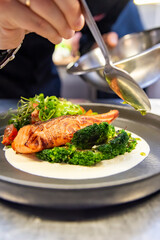 chef hand cooking salmon steak with broccoli and sauce on restaurant kitchen