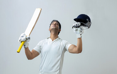 Indian man in cricket dress holding bat and helmet looking towards the sky celebrating century , cricket concept