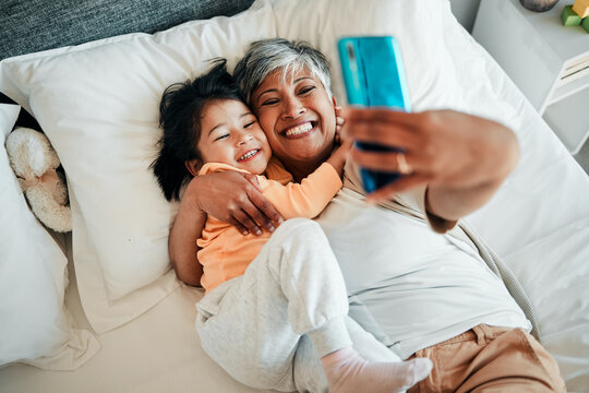Selfie, smile and grandmother with child on bed bonding, relax and love for happy family with care. Photography, technology and senior woman with little girl in bedroom on video call together in home