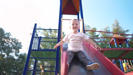 child slides down the slide on the playground. happy family kid dream concept. child son rides on a...