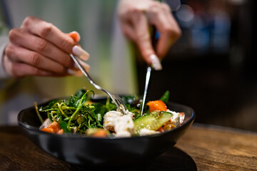 Woman's hands eat salad on table in restaurant