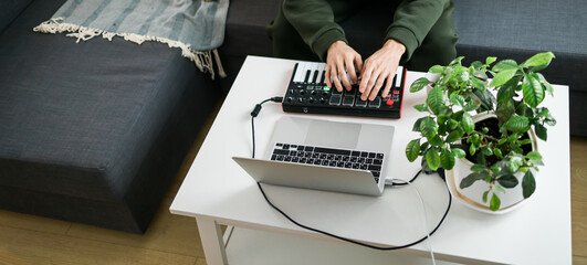 Man recording electronic music track with portable midi keyboard on laptop computer in home studio. Producing and mixing music beat making and arranging audio content with professional audio devices
