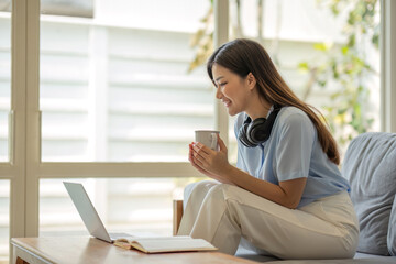 Fototapeta premium girl wearing headphones watching movies listening to music on laptop on the sofa at home on vacation with a cup of coffee