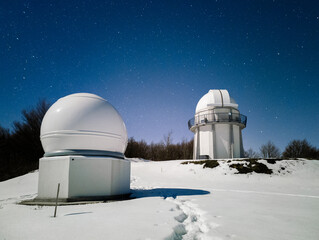 Telescope dome in snowy winter with the moon above at night