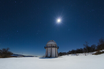 Telescope dome in snowy winter with the moon above at night