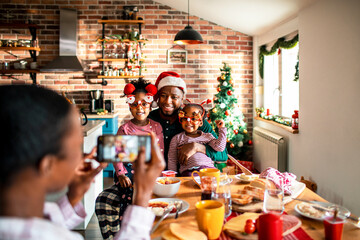 Young African American father posing for a picture with his daughters taken by his wife on a smartphone at their home decorated for the Christmas and new year holidays
