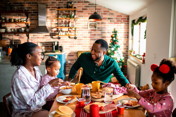 Young African American family having breakfast together in the morning at their home decorated for the Christmas and new year holidays