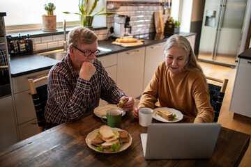 Senior couple having sandwiches together in the kitchen at home