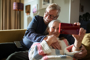 Senior Caucasian couple taking a selfie on a smartphone on the couch at home