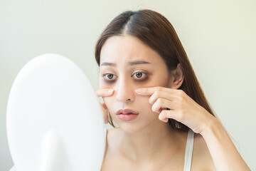 Bored, insomnia asian young woman, girl looking at mirror hand touching under eyes with problem of...