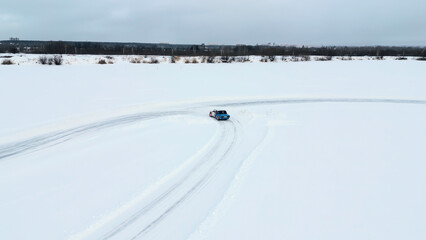 Aerial view of a frozen snow and ice covered lake with bending track. Clip. Drifting car on a...
