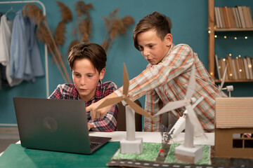 Homeschooling. Smart children work as a team using laptop computer to program wind turbines. Students learning about eco-friendly forms of renewable energy at home.