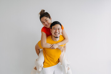 Happy Thai asian couple lover wear orange and yellow, woman riding piggyback on man back. Smiling and laughing, spending time together at apartment, isolated on white background. 