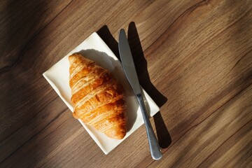Top view of croissant and knife on white plate on wooden table 