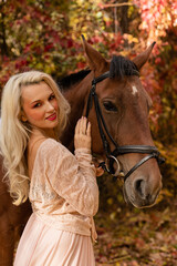 Fototapeta premium A woman in a long dress sits on a horse. Autumn forest, horse breeding