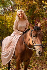 Fototapeta premium A woman in a long dress sits on a horse. Autumn forest, horse breeding