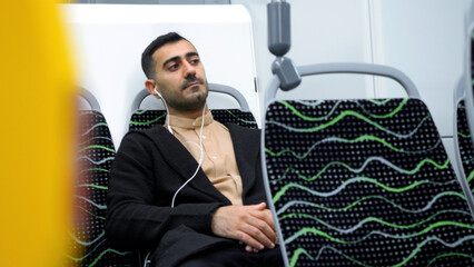 Man in public transport listening to music with white headphones. Media. Man sitting in empty bus...