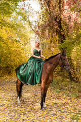 A woman in a long dress sits on a horse. Autumn forest, horse breeding