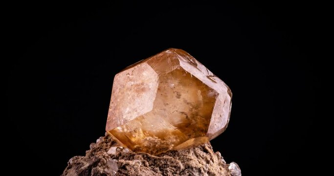 orange rhombohedral calcite on matrix 360&deg; loop rotating on black background. macro detail close-up rough raw unpolished semi-precious gemstone.
