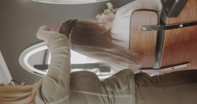 Combing the hair of a brunette lady prior to hair extensions attachment, vertical video, trucking