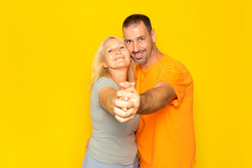 Caucasian married couple dancing a tango with hands stretched and faces together, isolated on yellow studio background.