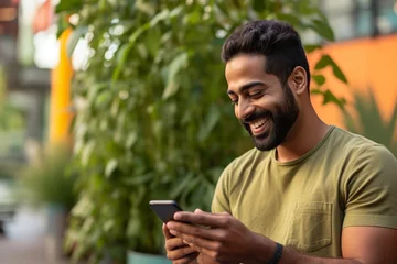 Papier Peint photo Magasin de musique A picture of a young indian man smiling and using his phone on a yellow background, black firday photo